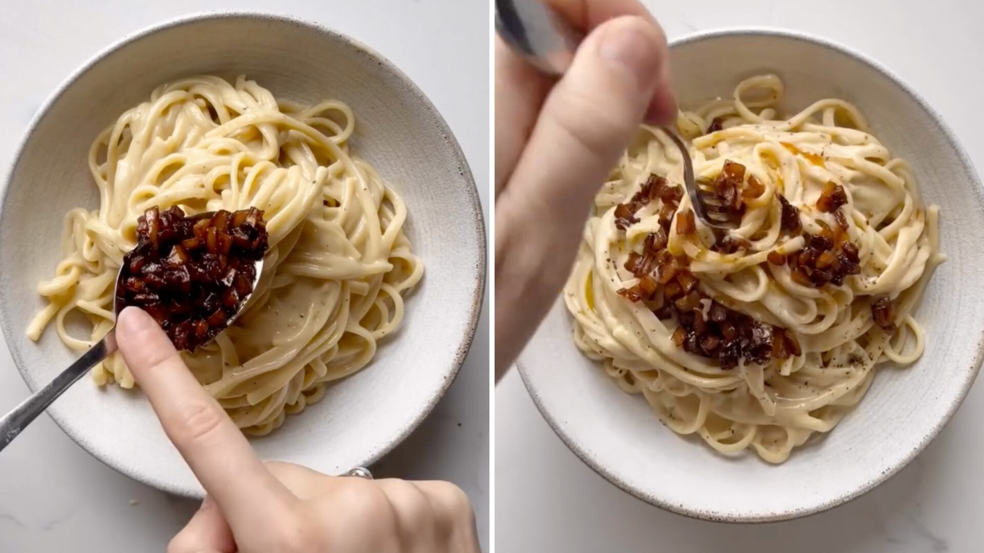 A bowl of creamy pasta topped with crispy bits, with a hand mixing in additional toppings.