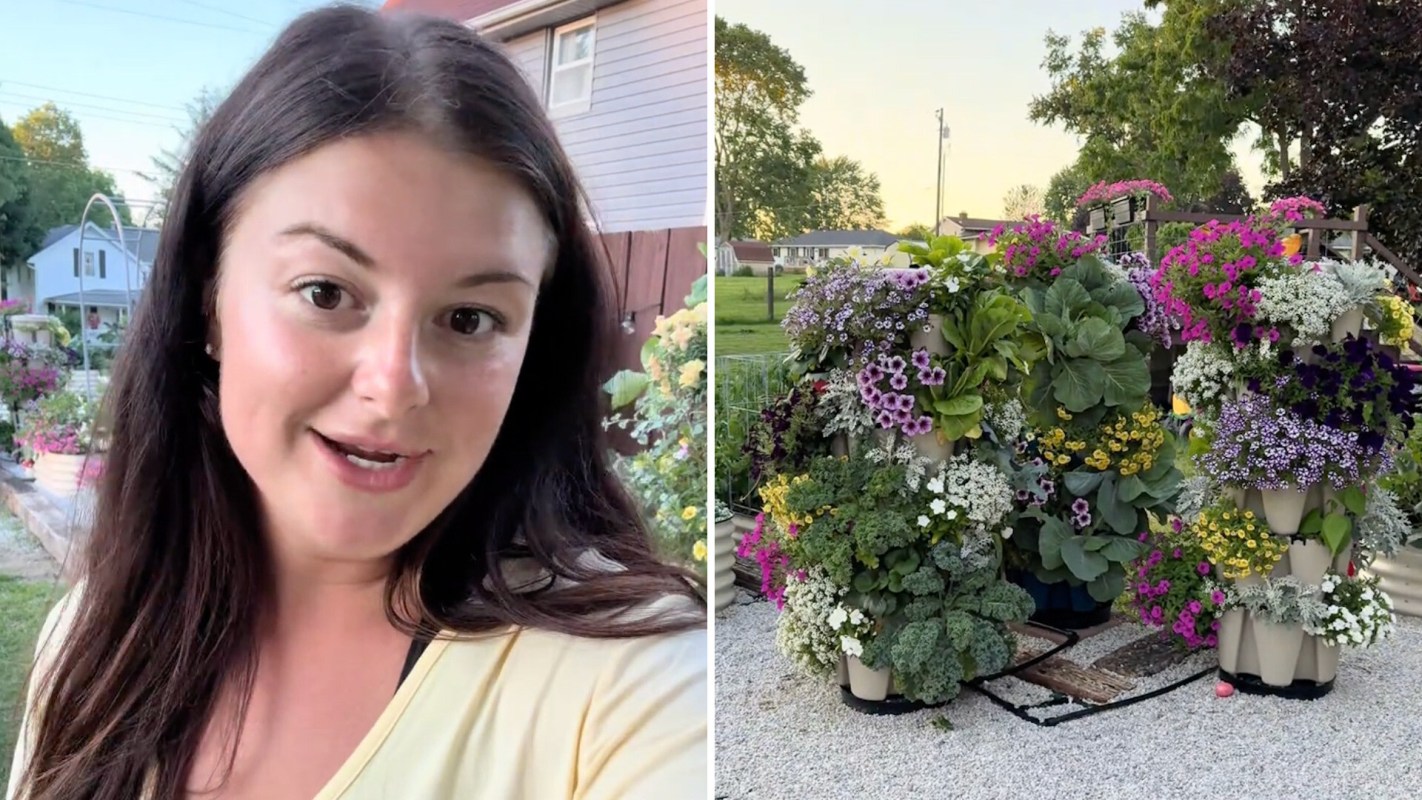 A woman in a yellow shirt smiles while showcasing a colorful vertical garden filled with various blooming flowers.