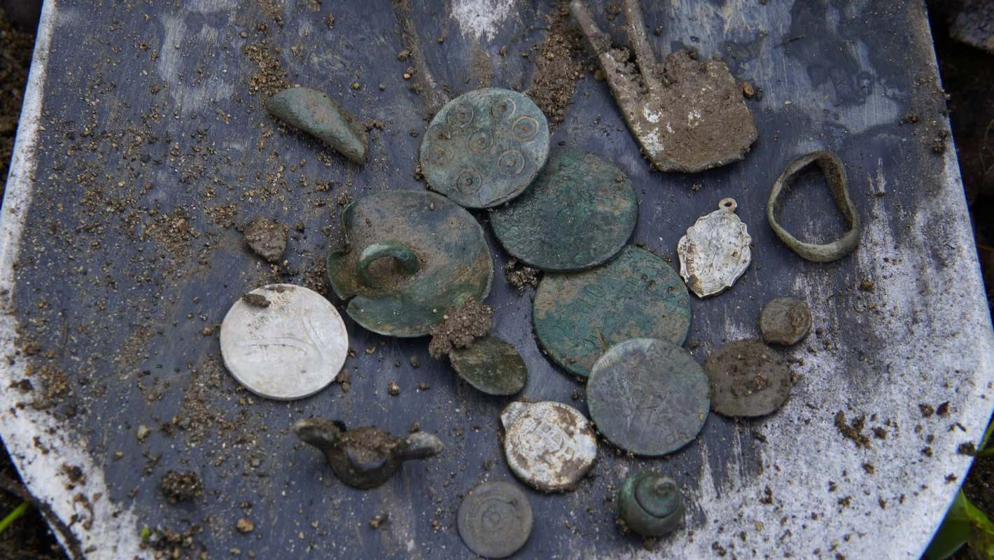 A collection of ancient coins and metal artifacts displayed on a shovel.