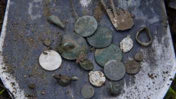 A collection of ancient coins and metal artifacts displayed on a shovel.