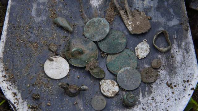 A collection of ancient coins and metal artifacts displayed on a shovel.