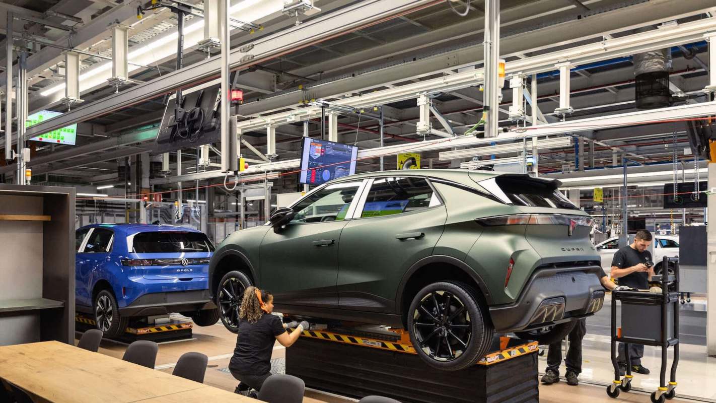 A worker inspects a green car in an automotive assembly plant with various other vehicles in the background.