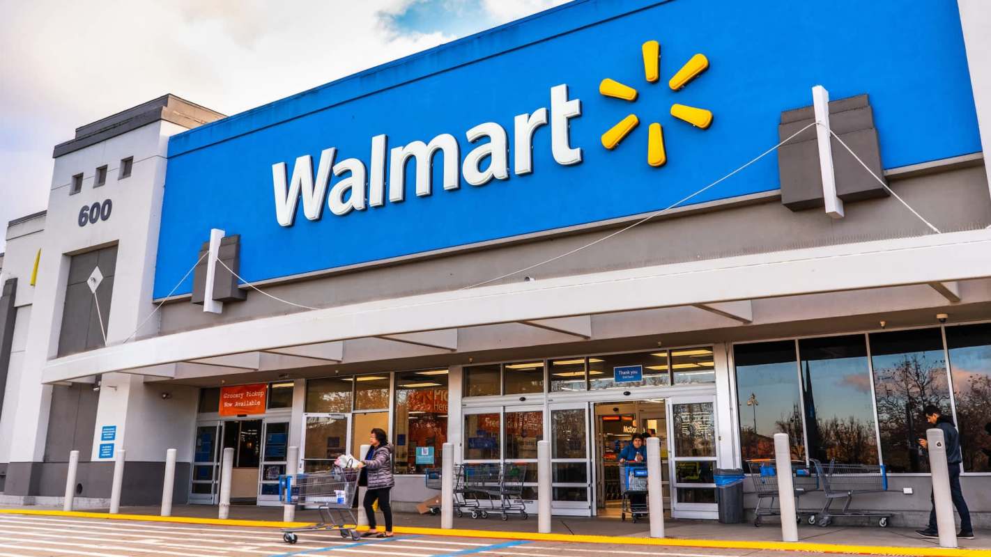 A Walmart store entrance with customers entering and exiting, featuring shopping carts outside.
