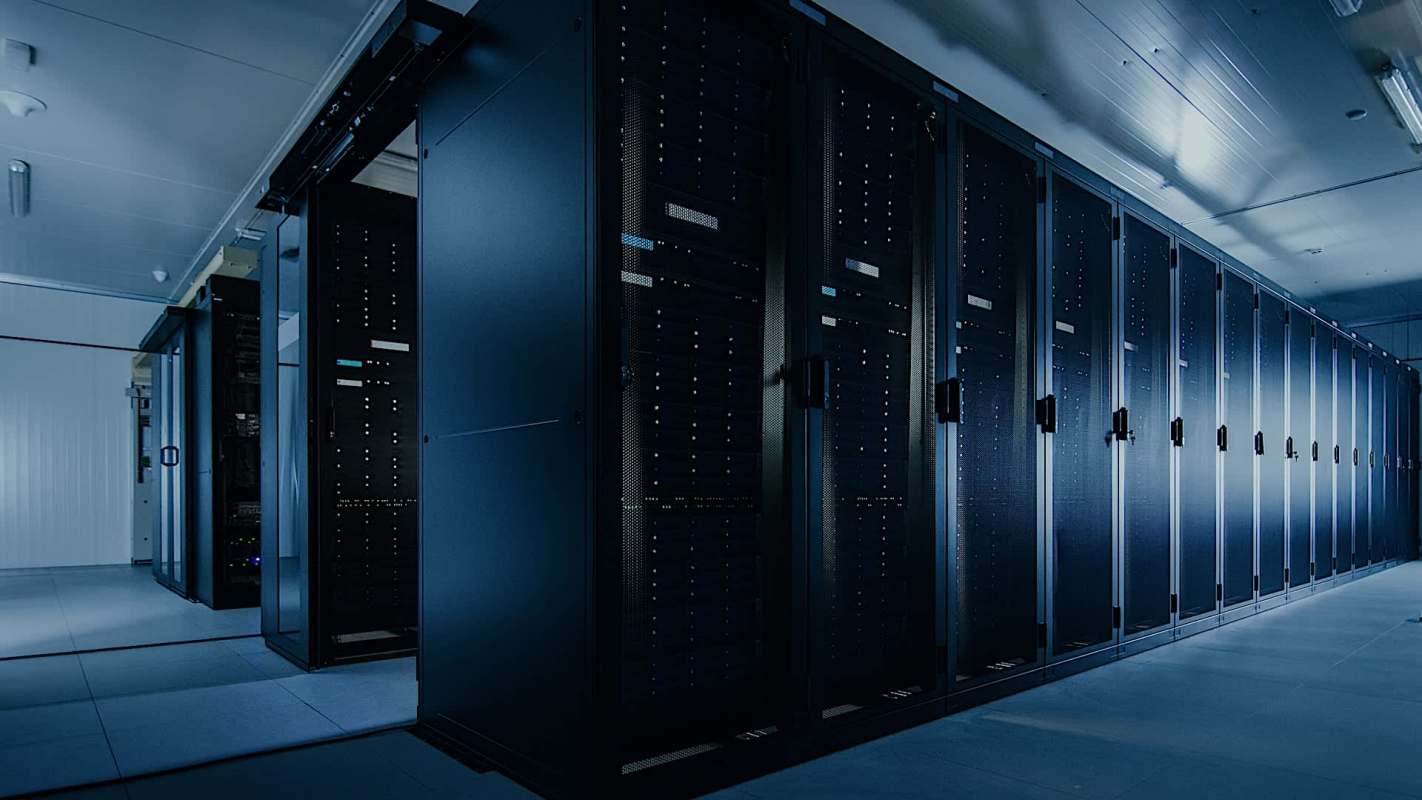 A dimly lit room filled with rows of server racks, showcasing various blinking indicators and dark cabinets.