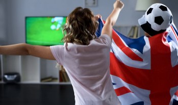 Two fans celebrating in front of a TV, one wrapped in a British flag.