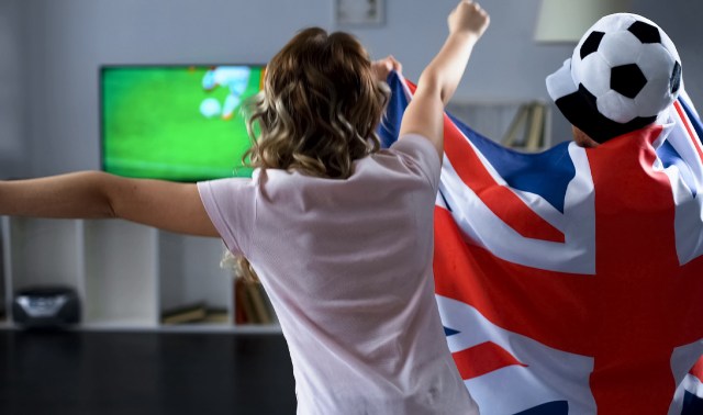 Two fans celebrating in front of a TV, one wrapped in a British flag.