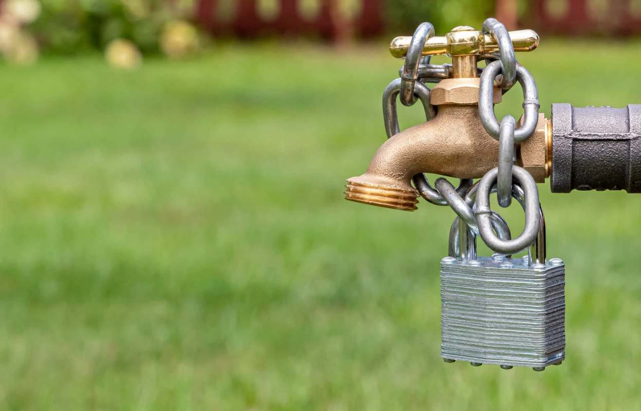 A brass faucet secured with a chain and padlock on a green grassy background.