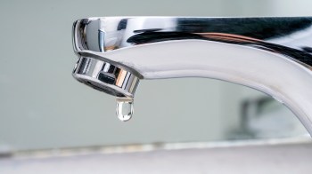 A close-up of a chrome faucet with a single droplet of water about to fall.