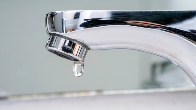 A close-up of a chrome faucet with a single droplet of water about to fall.