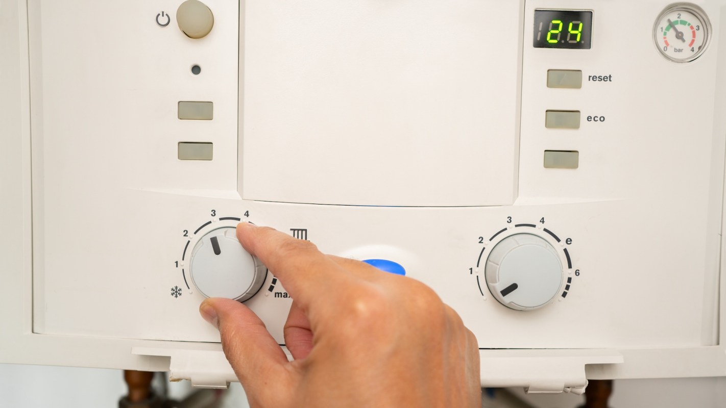 A hand adjusting the temperature dial on a white appliance with digital display and control buttons.