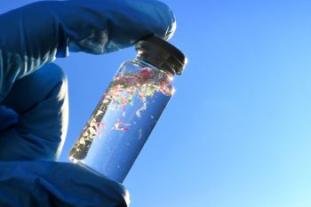 A gloved hand holds a glass vial containing plastic fragments.