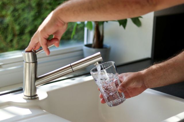 A person filling a glass with water in the kitchen.