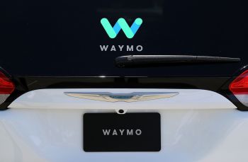 A close-up of a car's rear featuring the Waymo logo and a Chrysler emblem.
