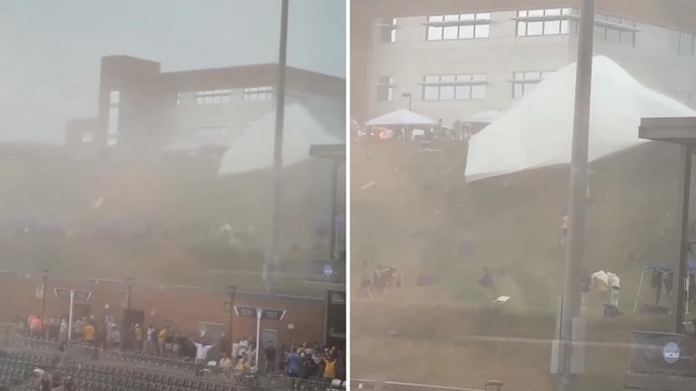 A misty scene shows a crowd by a sports venue as a large tent blows in strong winds.