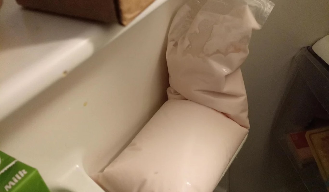 A bag of beige yogurt is sitting inside a refrigerator compartment next to a carton of milk.