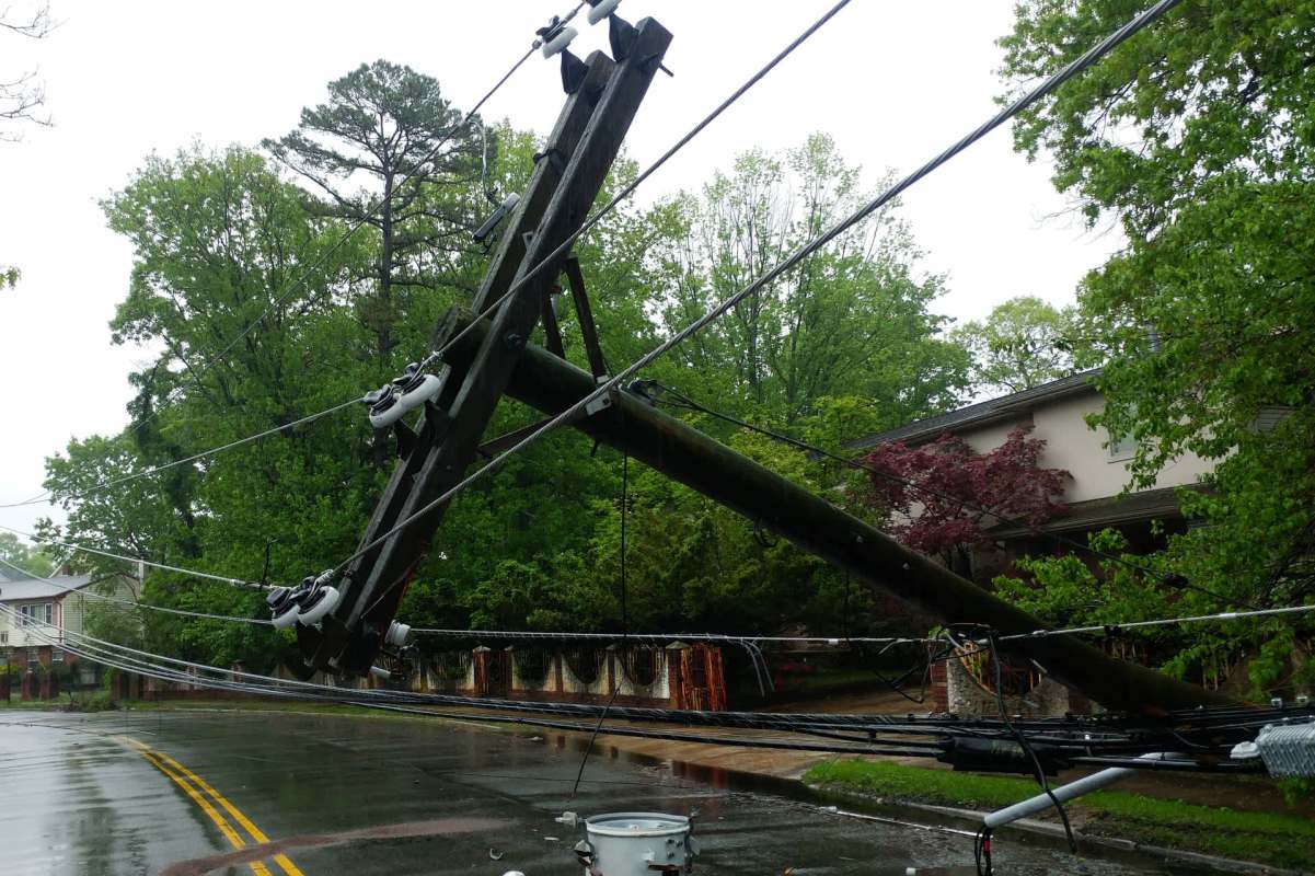 A fallen utility pole and downed power lines beside a wet road.