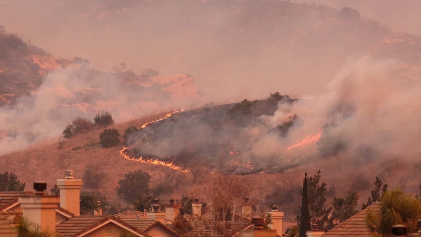 A hillside ablaze with flames and smoke, overlooking suburban rooftops.