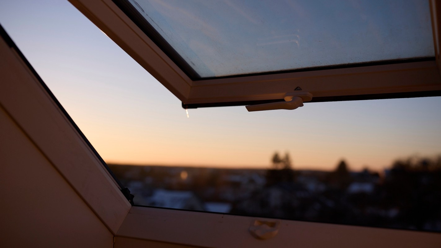 A partially open window reveals a sunset sky with vibrant hues and blurred landscape in the background.