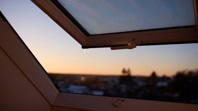 A partially open window reveals a sunset sky with vibrant hues and blurred landscape in the background.