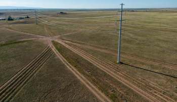 Aerial view of a rural landscape featuring intersecting dirt paths and a power line tower on flat terrain.