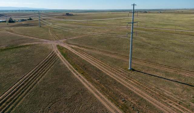 Aerial view of a rural landscape featuring intersecting dirt paths and a power line tower on flat terrain.