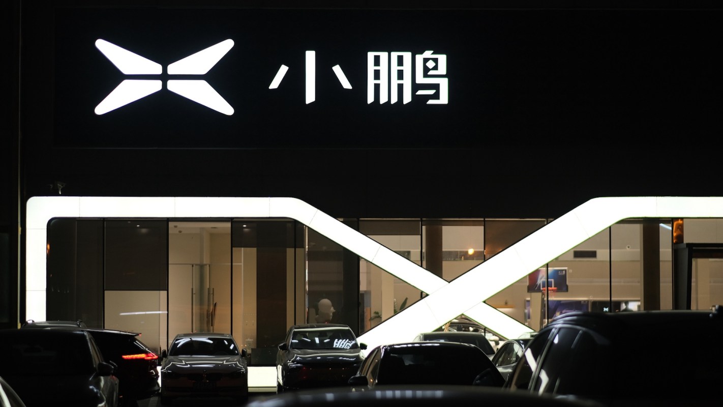 A brightly lit storefront featuring a Xpeng logo and several parked cars at night.