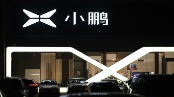 A brightly lit storefront featuring a Xpeng logo and several parked cars at night.
