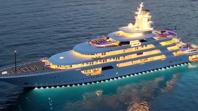 A luxurious yacht illuminated at night, gliding on serene waters with a clear blue hue beneath.