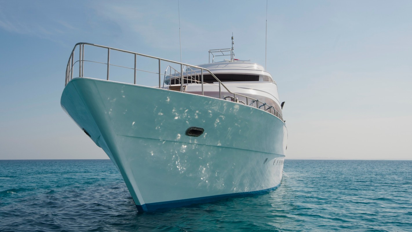 A luxury yacht anchored on clear blue water under a bright sky.