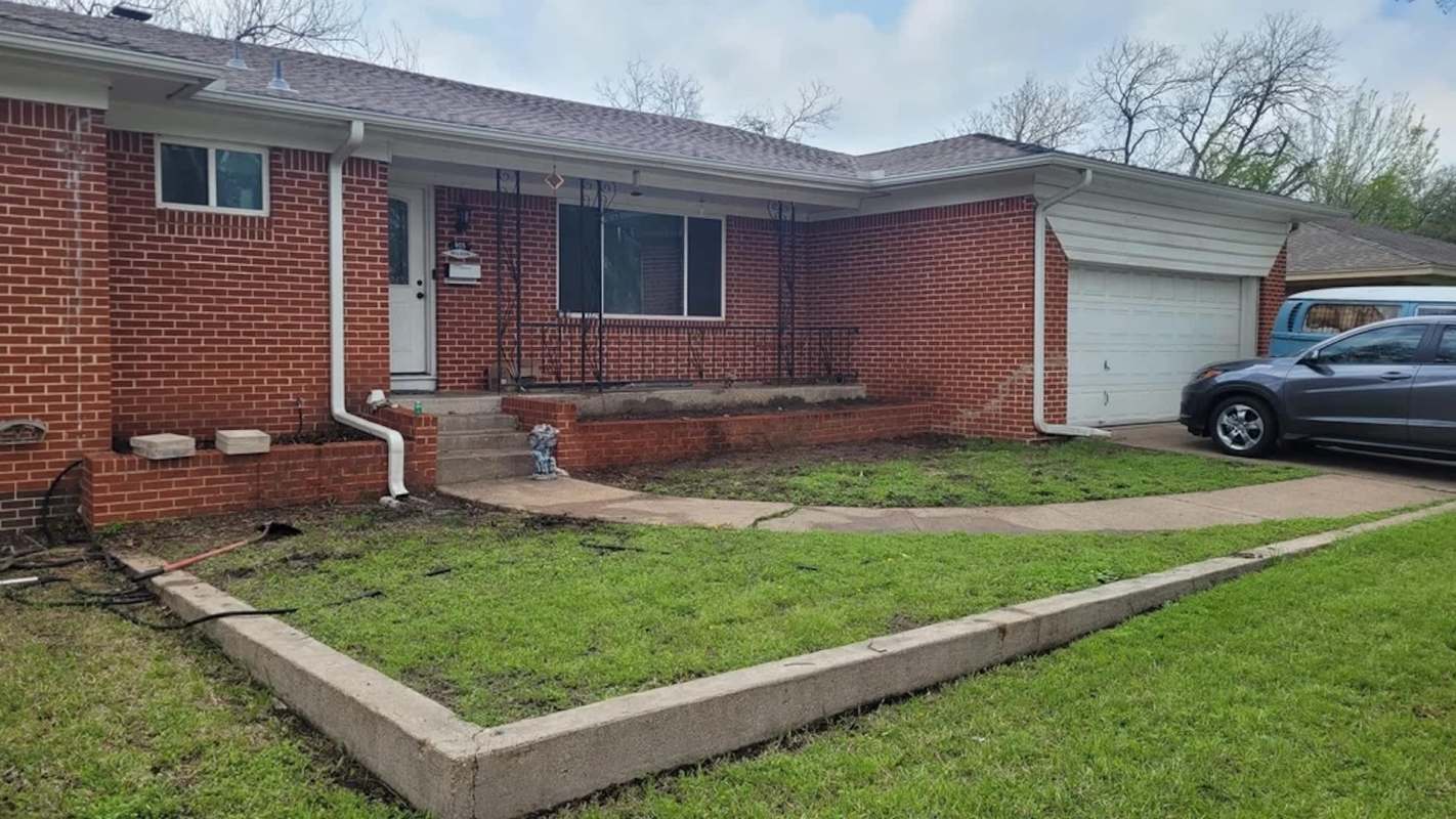 A brick house featuring a front porch, steps, a lawn, and a car parked in the driveway.