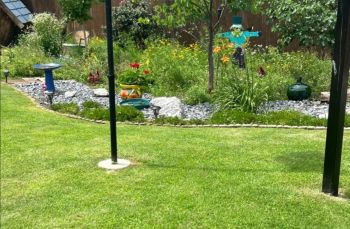 A lush garden featuring colorful flowers, decorative stones, a birdbath, and a whimsical scarecrow.