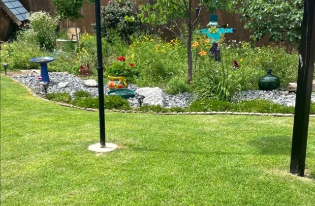 A lush garden featuring colorful flowers, decorative stones, a birdbath, and a whimsical scarecrow.