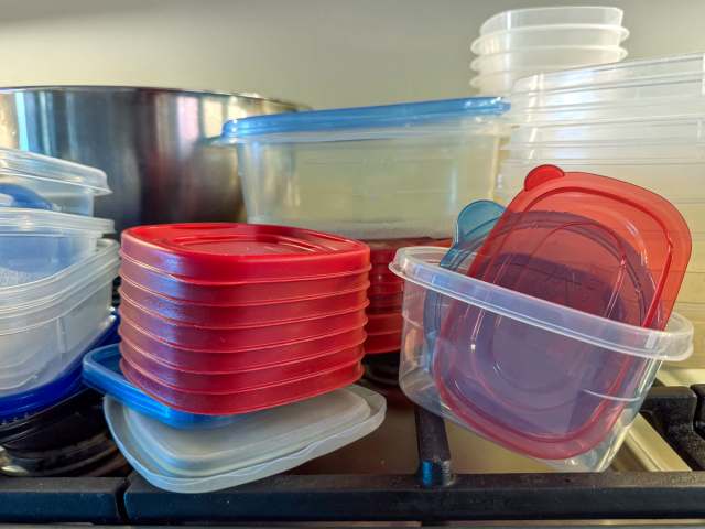 A stack of plastic food storage containers in various sizes and colors resting on a gas stovetop.