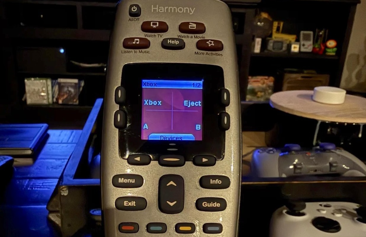 A Harmony universal remote displaying the Xbox control interface on its screen, with various buttons visible.