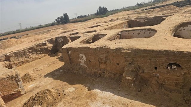 An archaeological site featuring large, exposed earth structures and shallow pits under a clear sky.