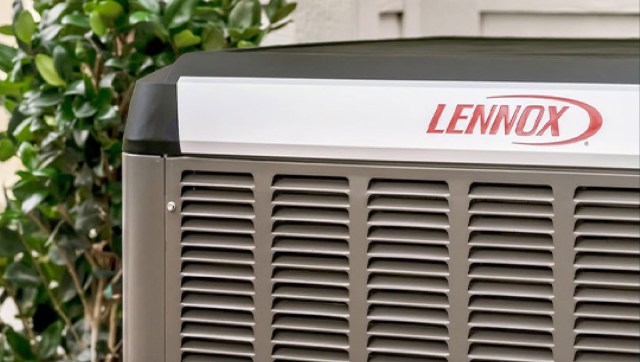 A Lennox outdoor heat pump unit beside green foliage.