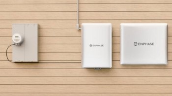 A wall-mounted electricity meter and two Enphase energy units on a wooden-paneled surface.