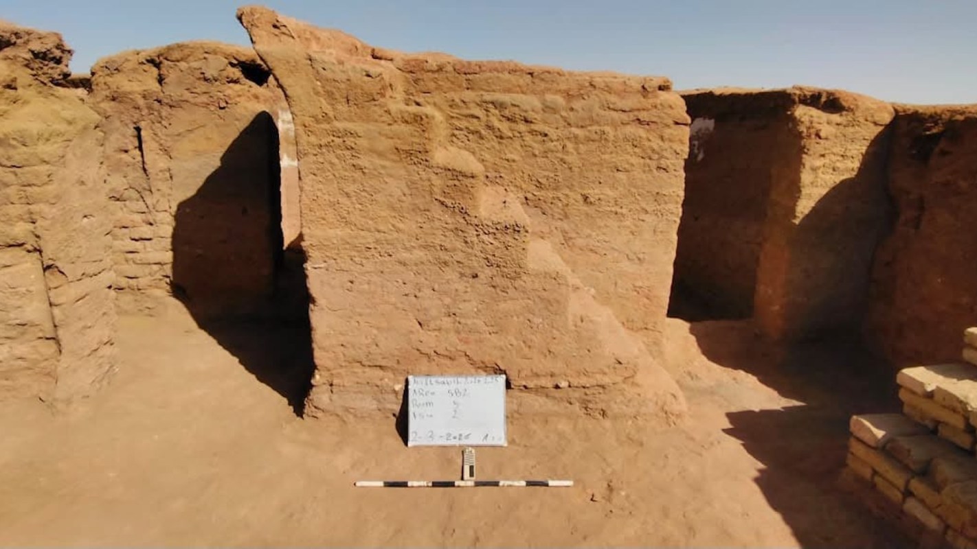 An excavated ancient structure with mud walls and a sign indicating its archaeological details.