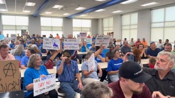 A crowded meeting with attendees holding anti-data center signs.
