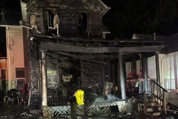 A burned and damaged house with charred wood and debris visible in the front.