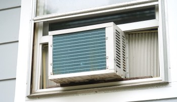 An air conditioning unit is installed in a partially open window, with external fins visible.
