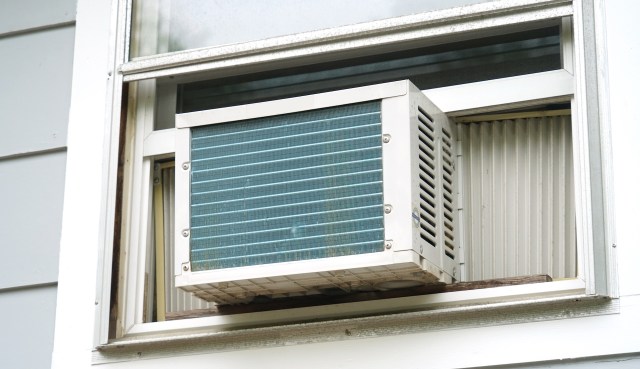 An air conditioning unit is installed in a partially open window, with external fins visible.