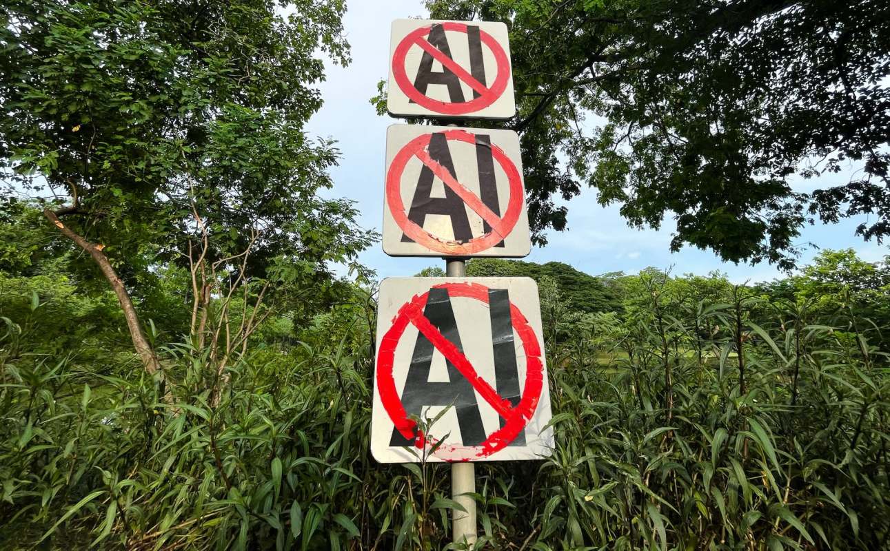 Three signs displaying "AI" crossed out with red circles, surrounded by greenery and trees.