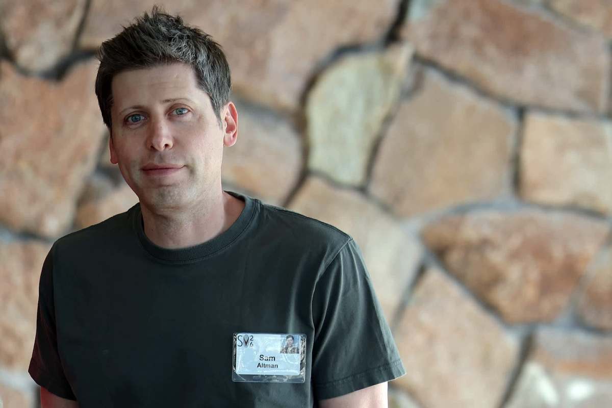 A man stands in front of a stone wall, wearing a name tag and a dark shirt.