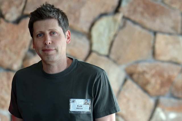 A man stands in front of a stone wall, wearing a name tag and a dark shirt.