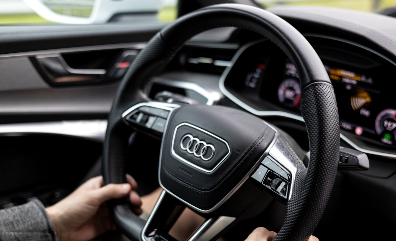 A person with their hands on an Audi steering wheel.