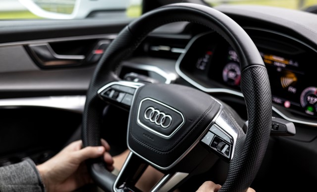 A person with their hands on an Audi steering wheel.