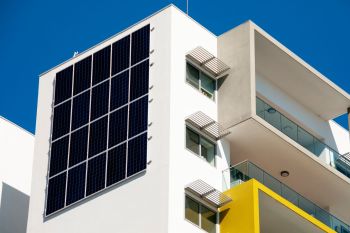 A modern building featuring large solar panels on its side against a clear blue sky.
