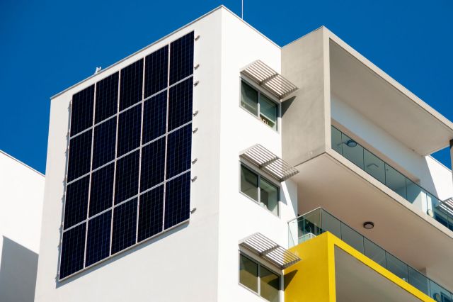 A modern building featuring large solar panels on its side against a clear blue sky.