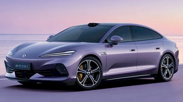A sleek purple electric car parked by the water against a pastel sunset backdrop.